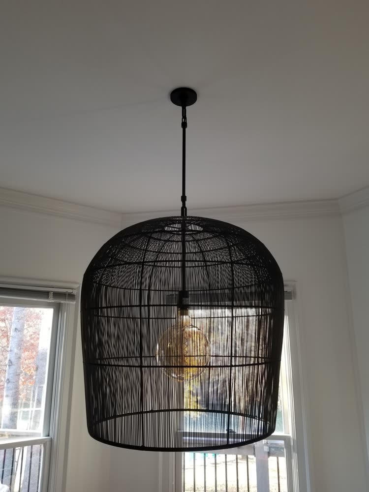 Black wire-cage pendant light hung from a ceiling in a bay window, lit with an exposed globe bulb