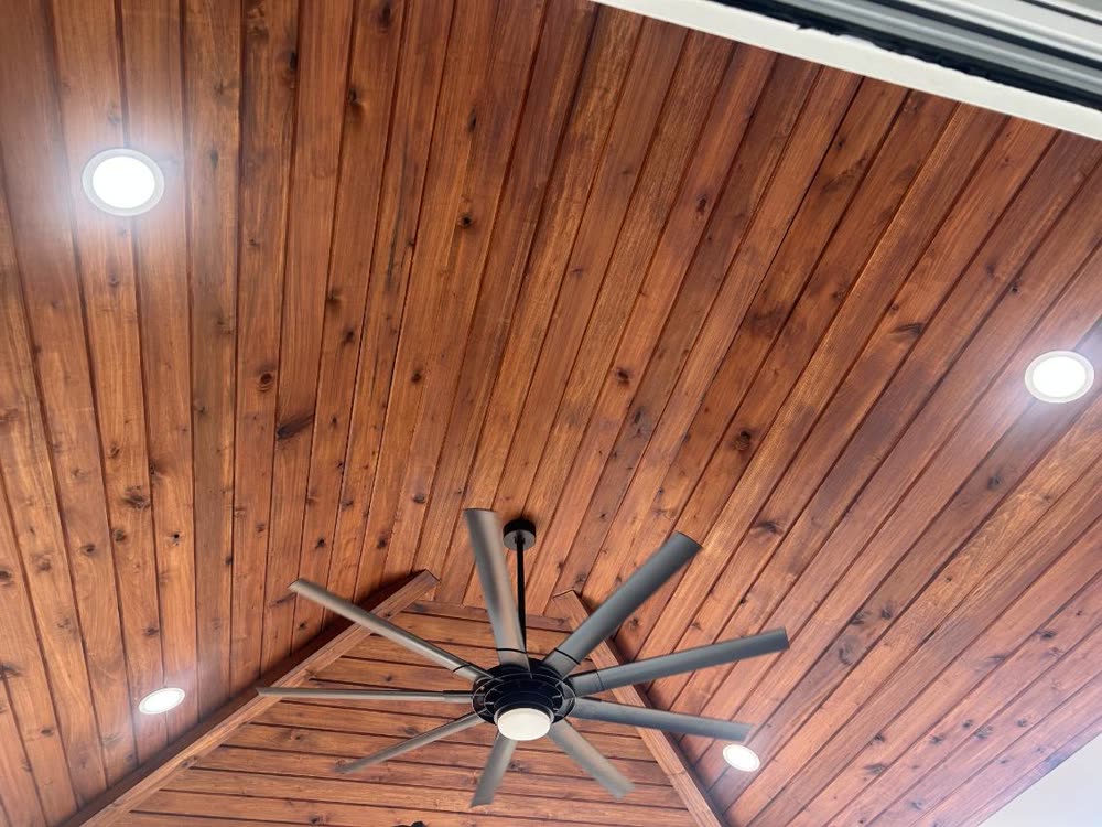 Large ceiling fan and recessed can lights installed in a stained tongue-and-groove wood porch ceiling